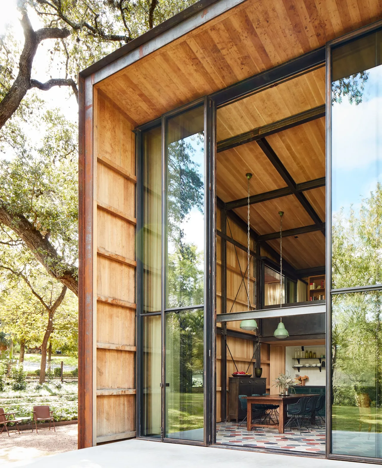Jewell Box features rust patina steel framing with large glass doors opening to a wooded outdoor setting.