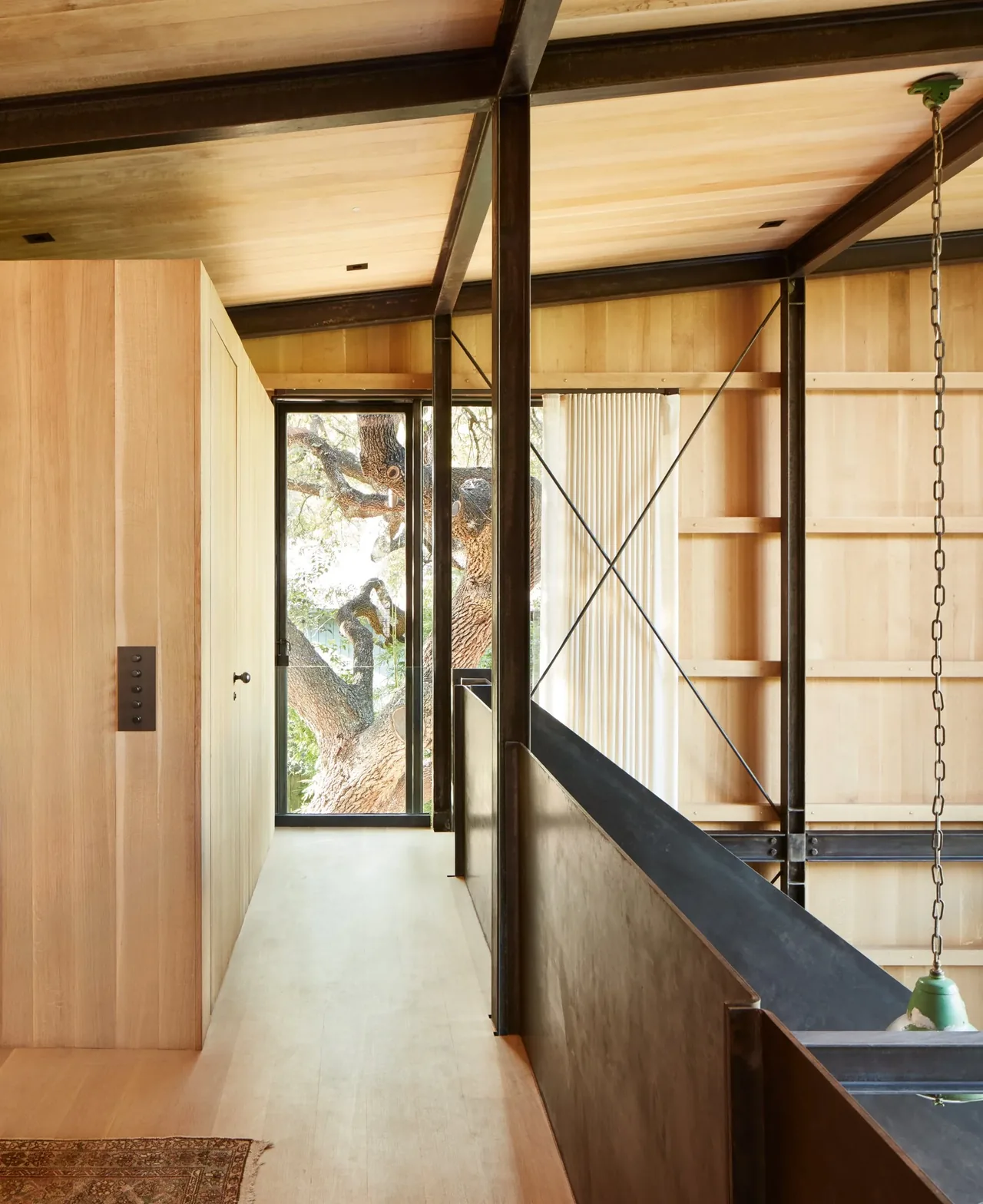 Hallway featuring light wood paneling and exposed black steel cross braces with a window view of tree branches.