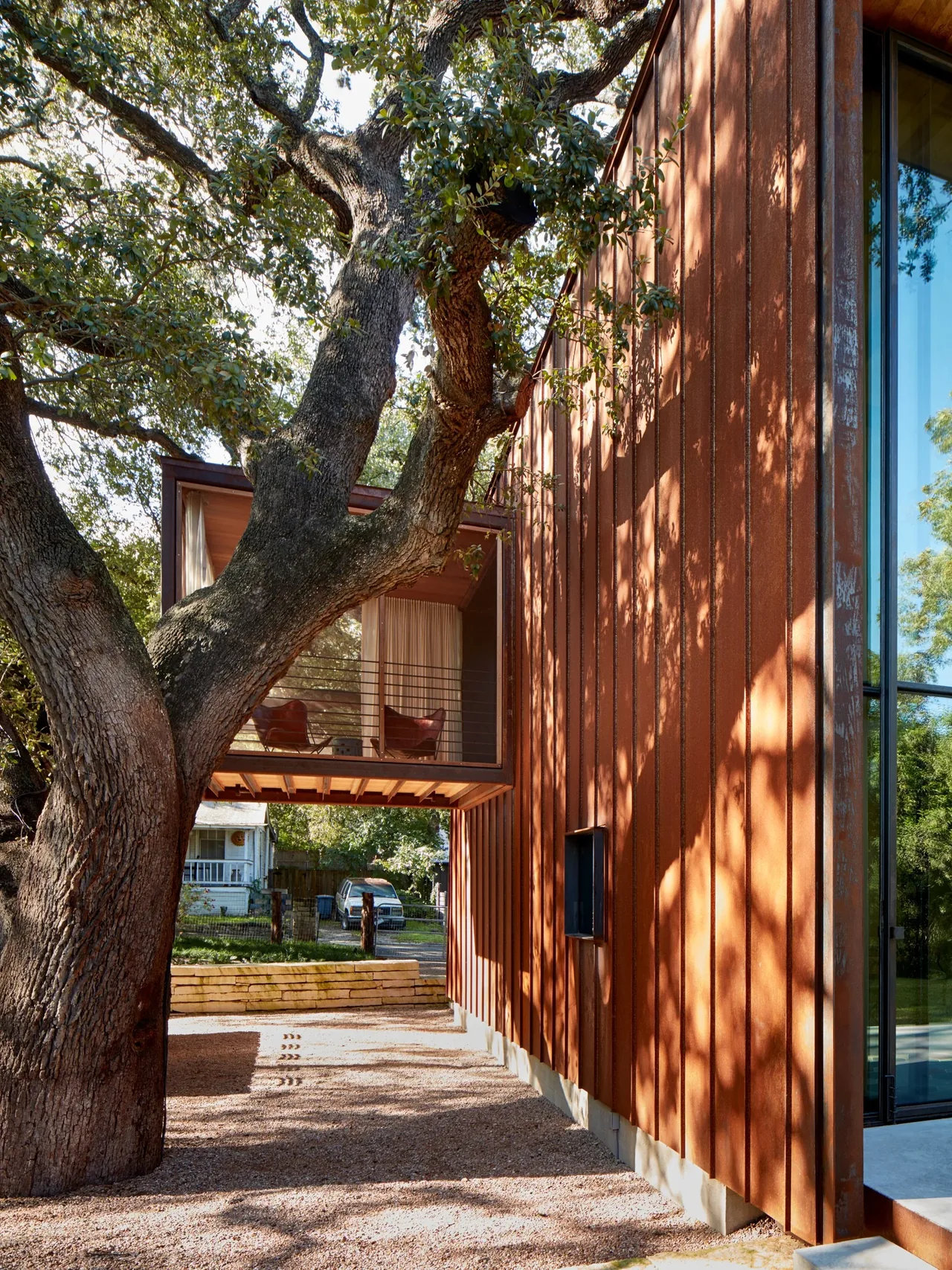 Jewell Box residence exterior features rust patina steel siding with an elevated glassed balcony nestled among large oak trees.