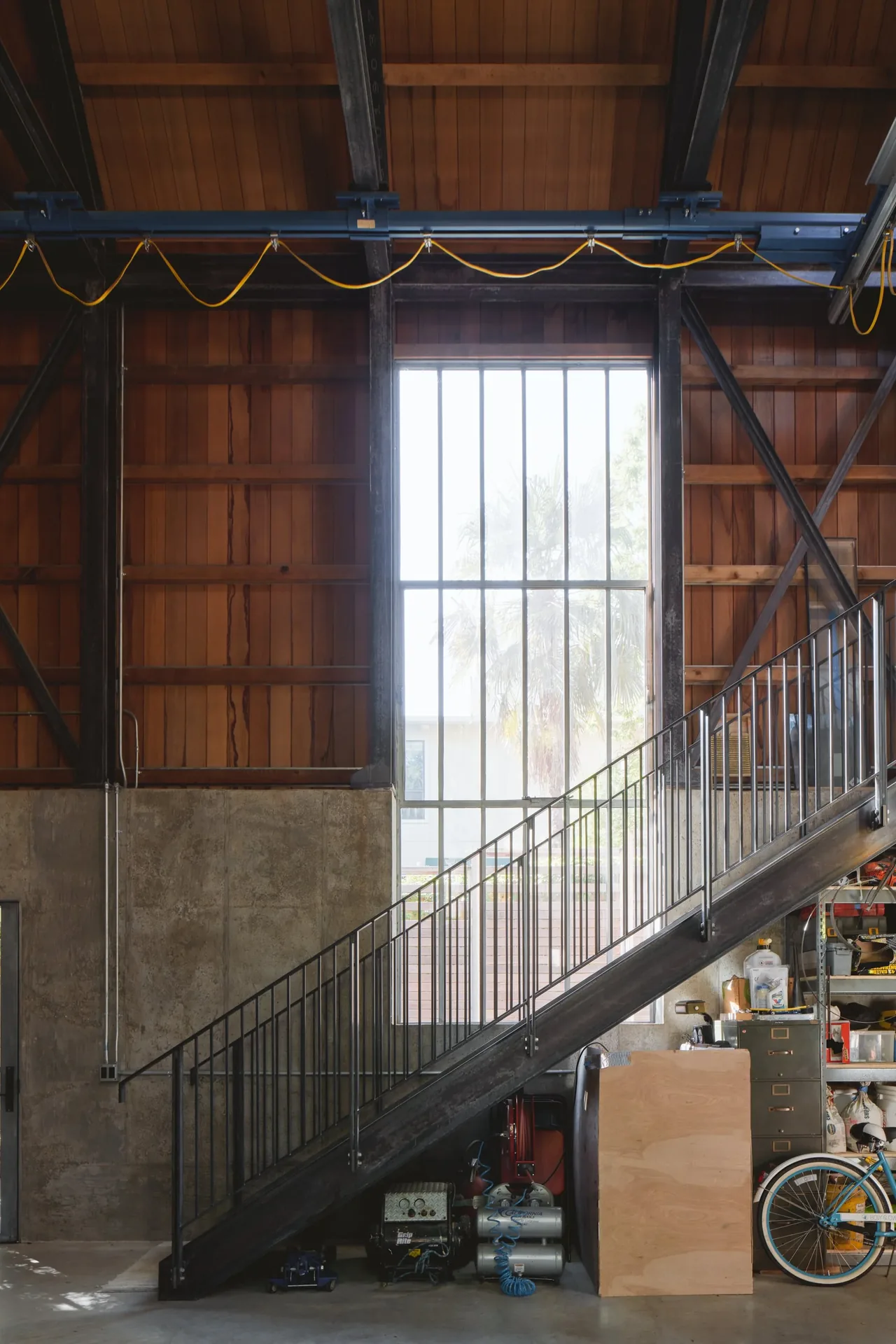 Industrial interior showing a metal staircase against a backdrop of wood paneling and concrete walls with a large vertical grid window.