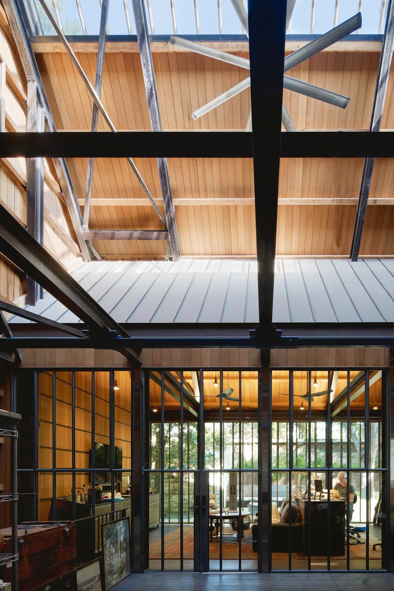 Office space features vertical wood paneling, metal grid windows, and exposed steel beams under a skylight roof.