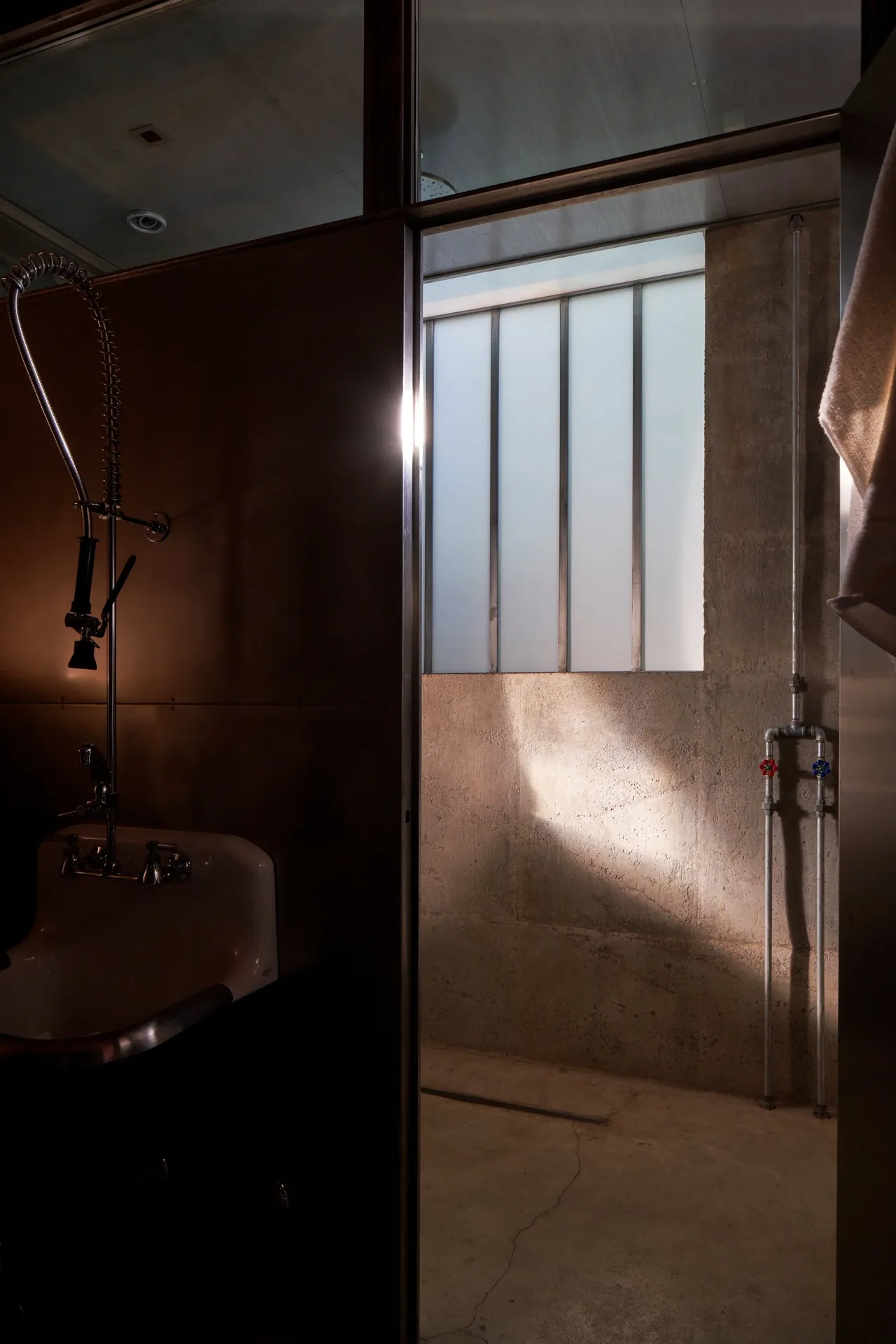 Industrial style bathroom features exposed concrete walls and stainless steel vintage faucet with flexible hose.