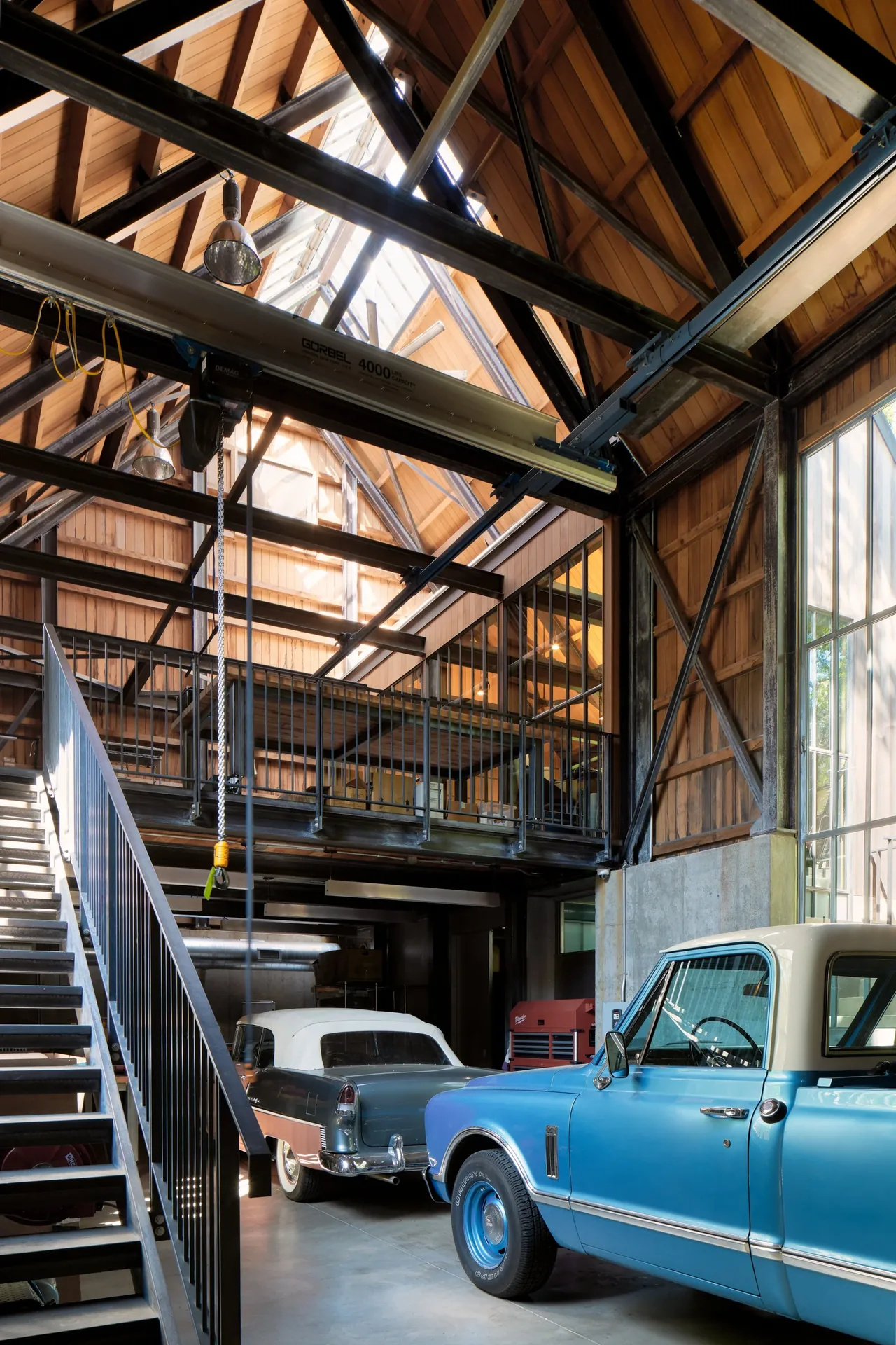 Garage interior with exposed timber framing, a metal staircase, and two classic automobiles parked inside.