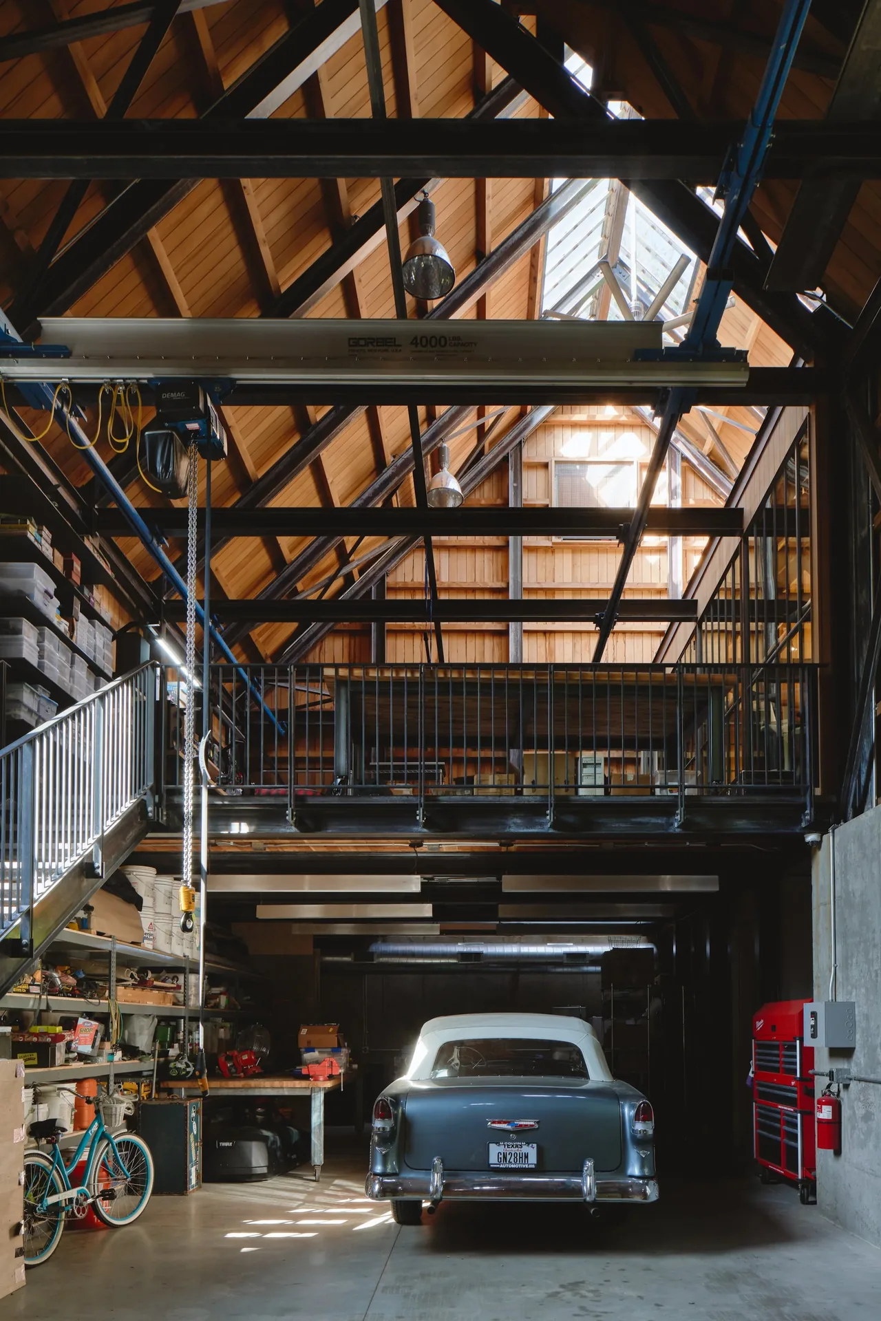 Garage interior featuring a vintage car, loft with metal railing, and exposed wooden roof trusses with skylights.
