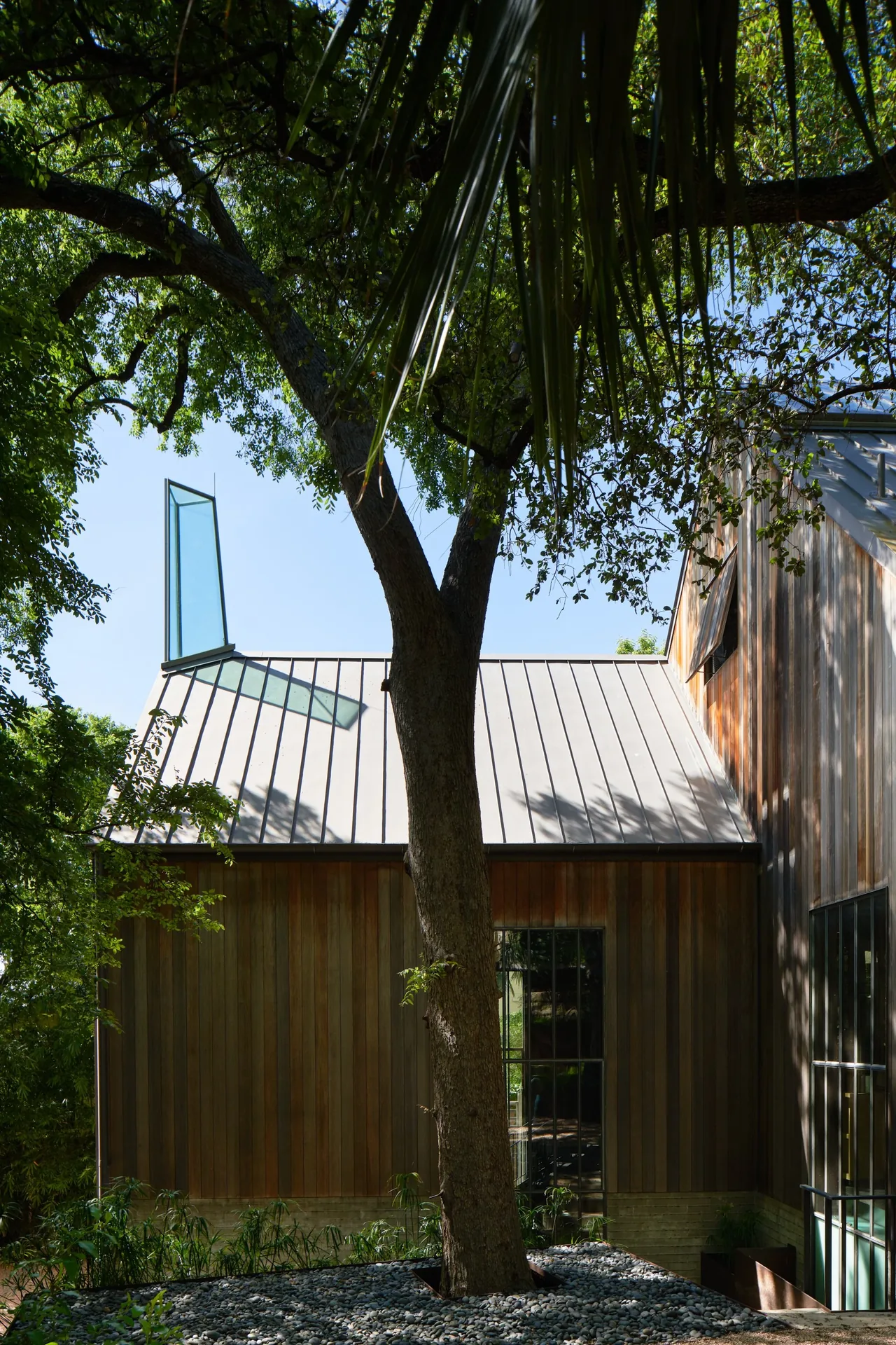Narrow house with vertical wood siding, metal standing seam roof, and a vertical glass chimney element.