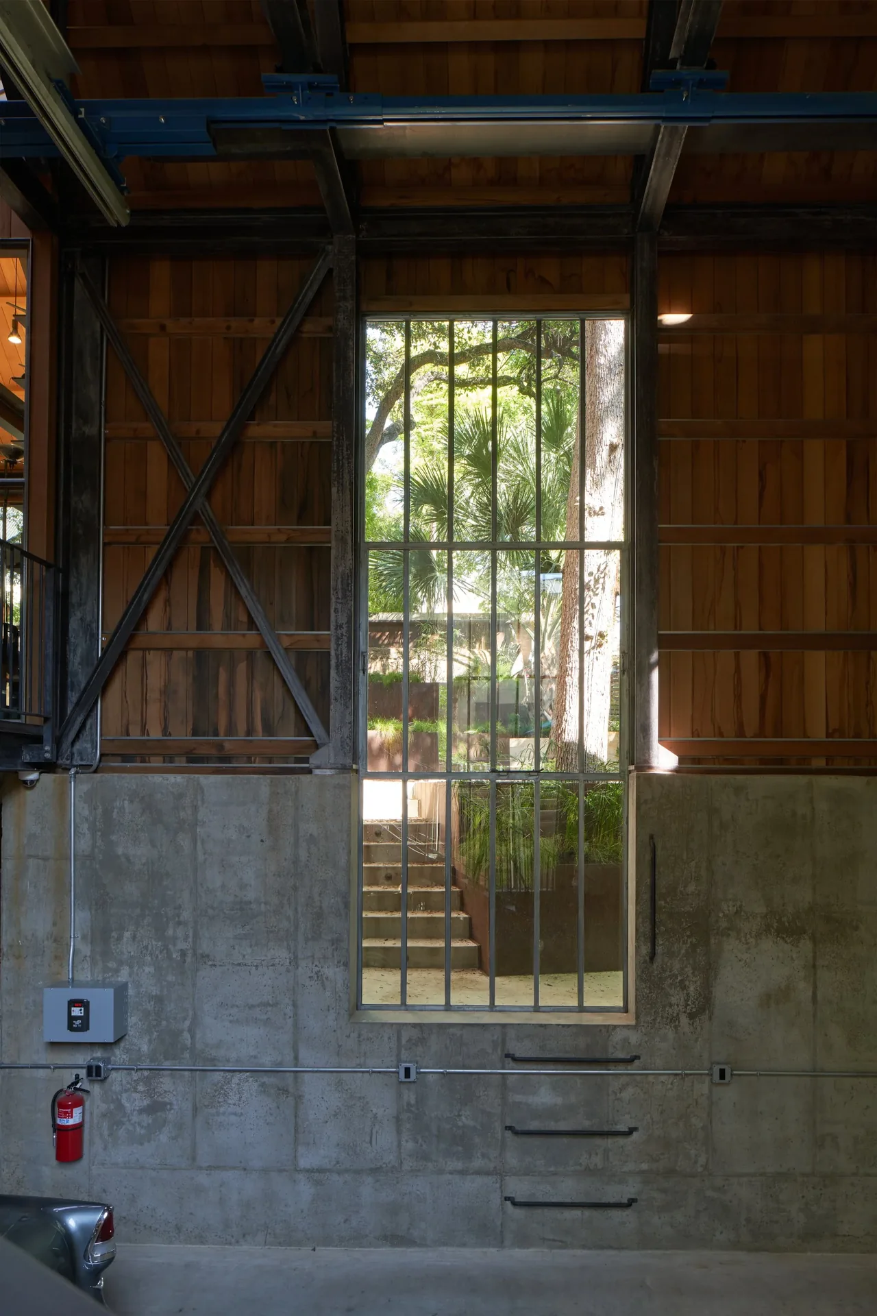 Interior wall with floor-to-ceiling vertical grid window and combination of concrete base and vertical wood siding above.