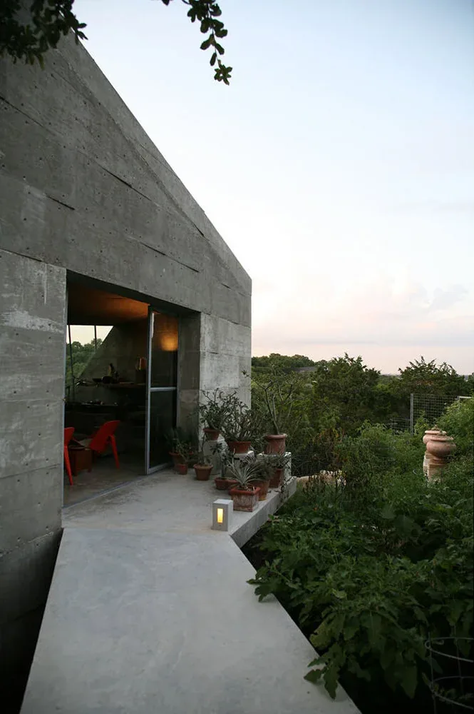 Concrete Studio Gallery features textured concrete walls, potted plants, and a small rectangular window with a surrounding natural landscape.