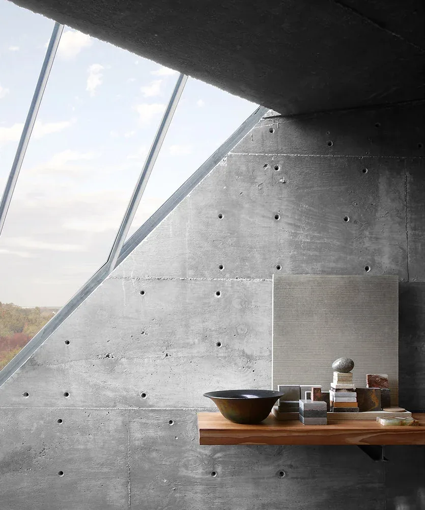 Interior featuring a textured concrete wall with a small rectangular window and a simple wooden shelf with objects.