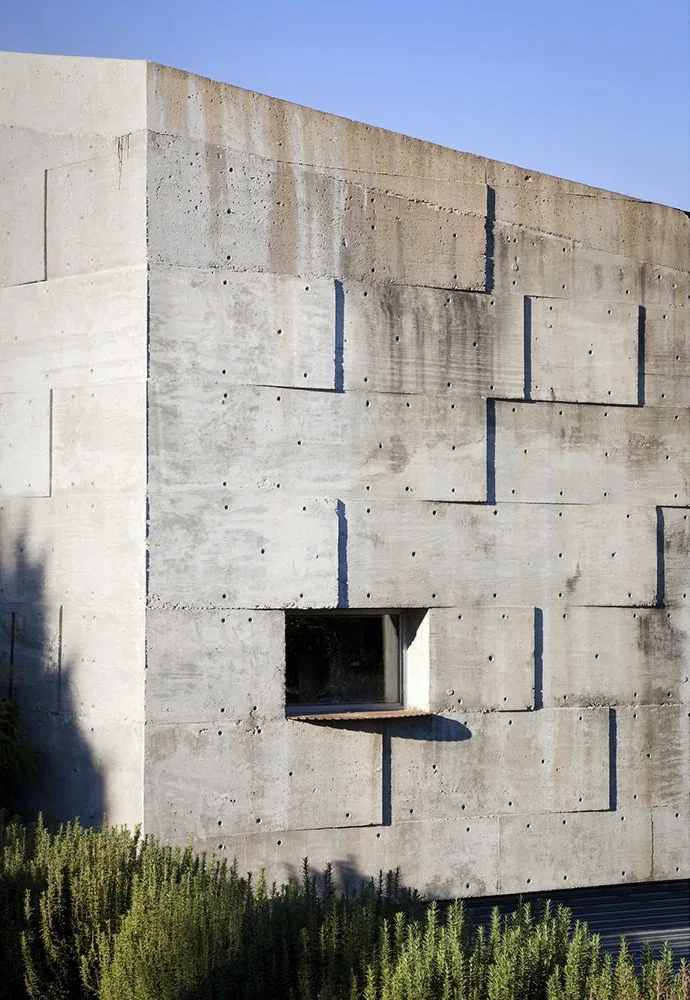 Textured concrete exterior wall features a small rectangular window casting a shadow at the Concrete Studio Gallery.