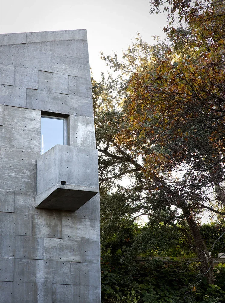 Textured concrete wall with small rectangular window and cantilevered balcony at Concrete Studio Gallery.