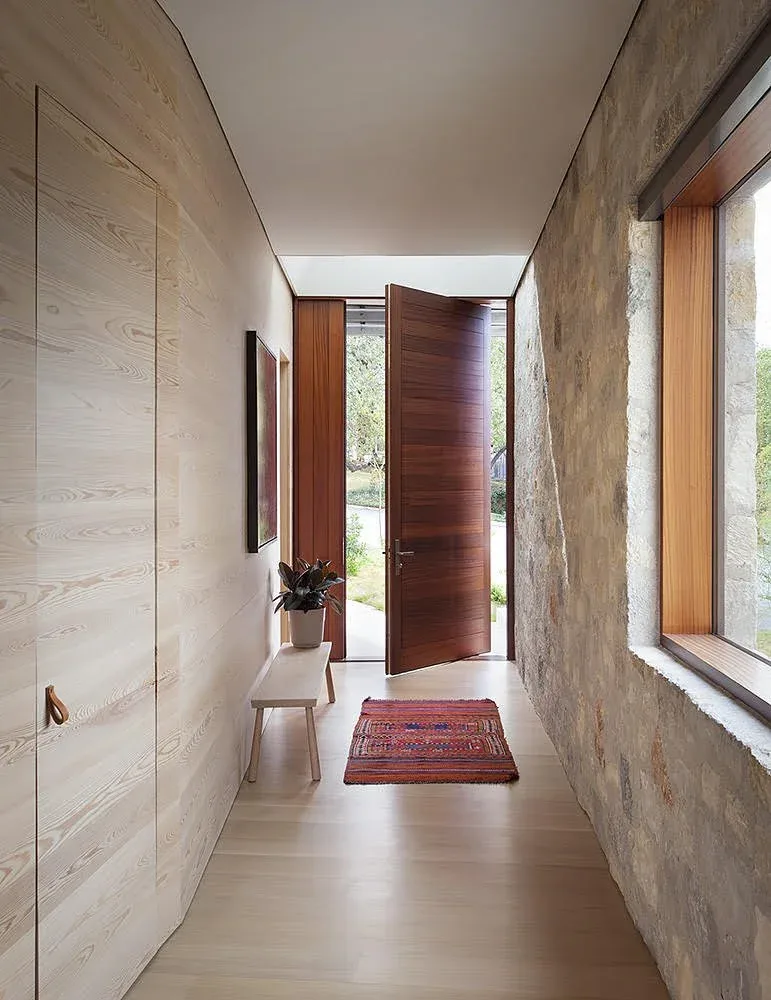 Entry hallway with a combination of stone and wood wall finishes, a wooden pivot door, and a window overlooking the front yard.