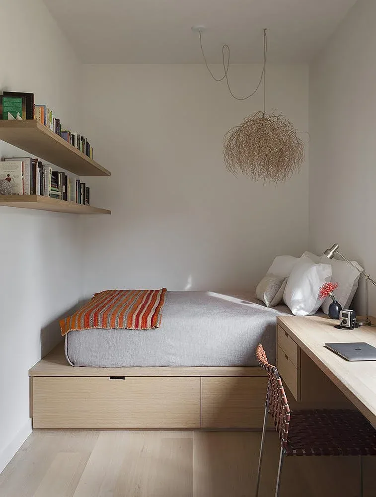 Compact bedroom with built-in platform bed and desk showcasing wood tones and a woven pendant light.