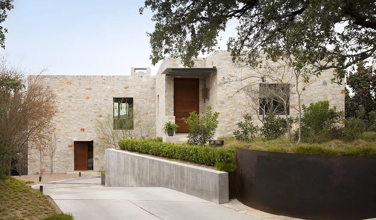 556 House features a stone exterior with wood doors and a modern concrete driveway.