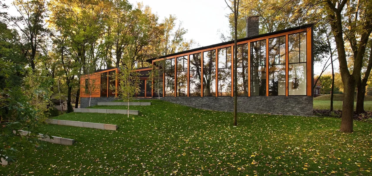 Farquar Lake Residence features large vertical windows with wood framing and a stone base set in a wooded landscape.