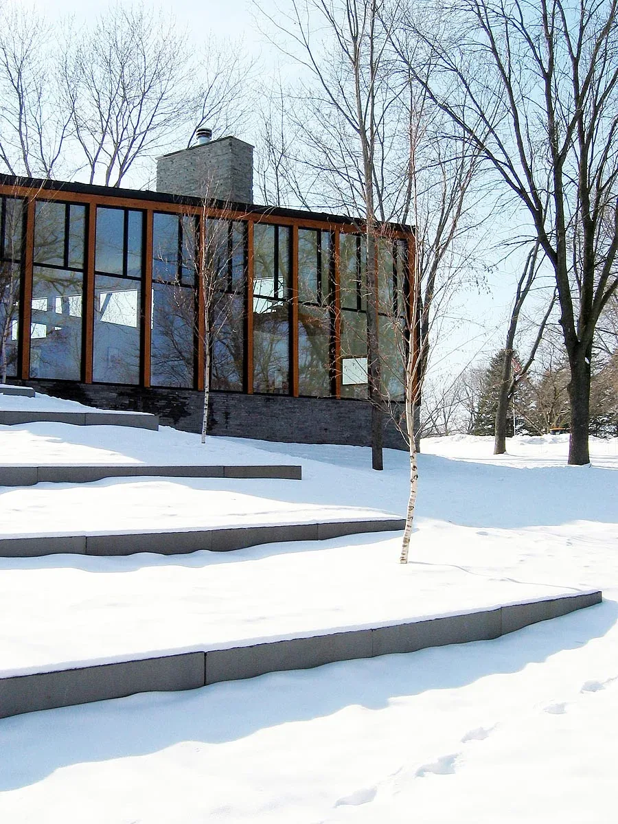 Exterior rear view of Farquar Lake Residence showing terraced snow-covered landscaping and large floor-to-ceiling windows.