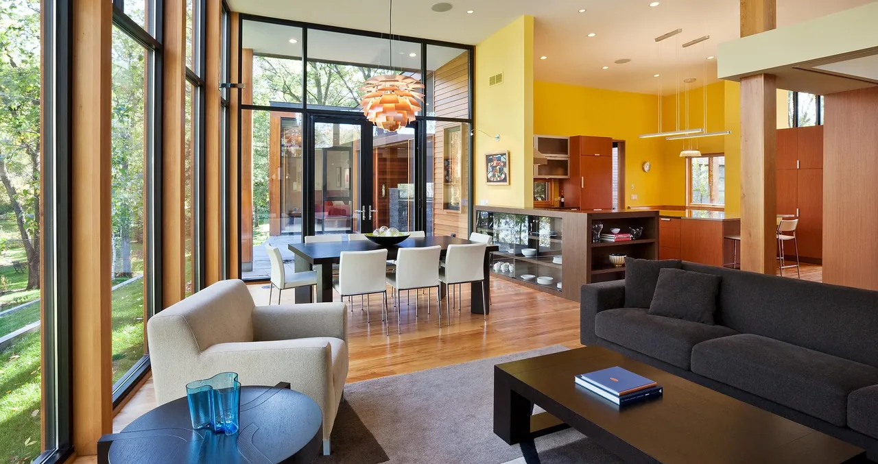 Open living and dining space with wood framed floor-to-ceiling glazing and a view of the outdoors.