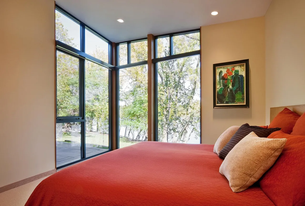 Corner bedroom with floor-to-ceiling corner windows offering lake views and a colorful painting on the wall.