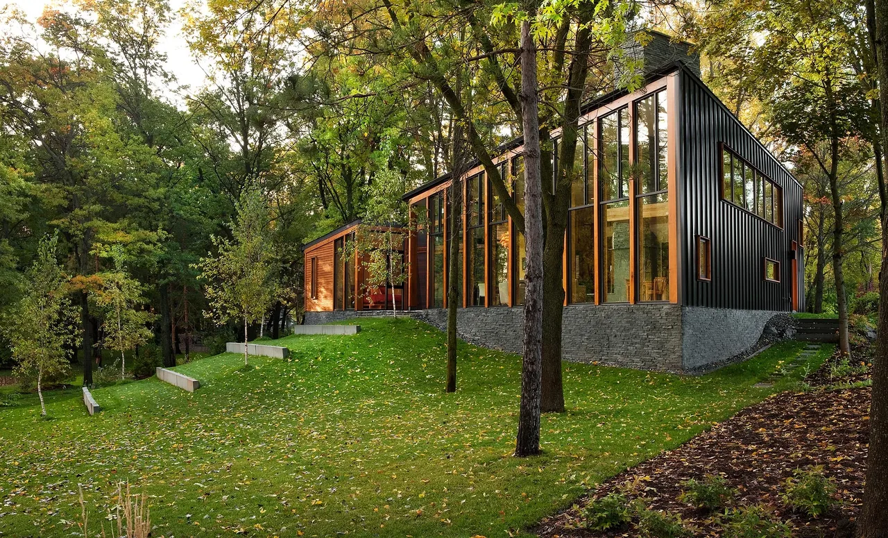 Farquar Lake Residence features a modern design with vertically oriented windows and black metal siding on a stone base in a wooded setting.
