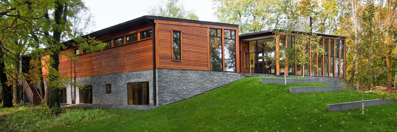 Farquar Lake Residence features a stone foundation, vertical wood siding, and floor-to-ceiling windows on a sloped yard with terraced walls.
