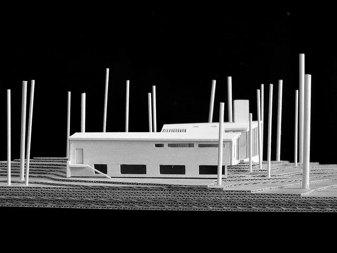 White architectural model showing a modern flat-roofed house with narrow clerestory windows and layered topography base.