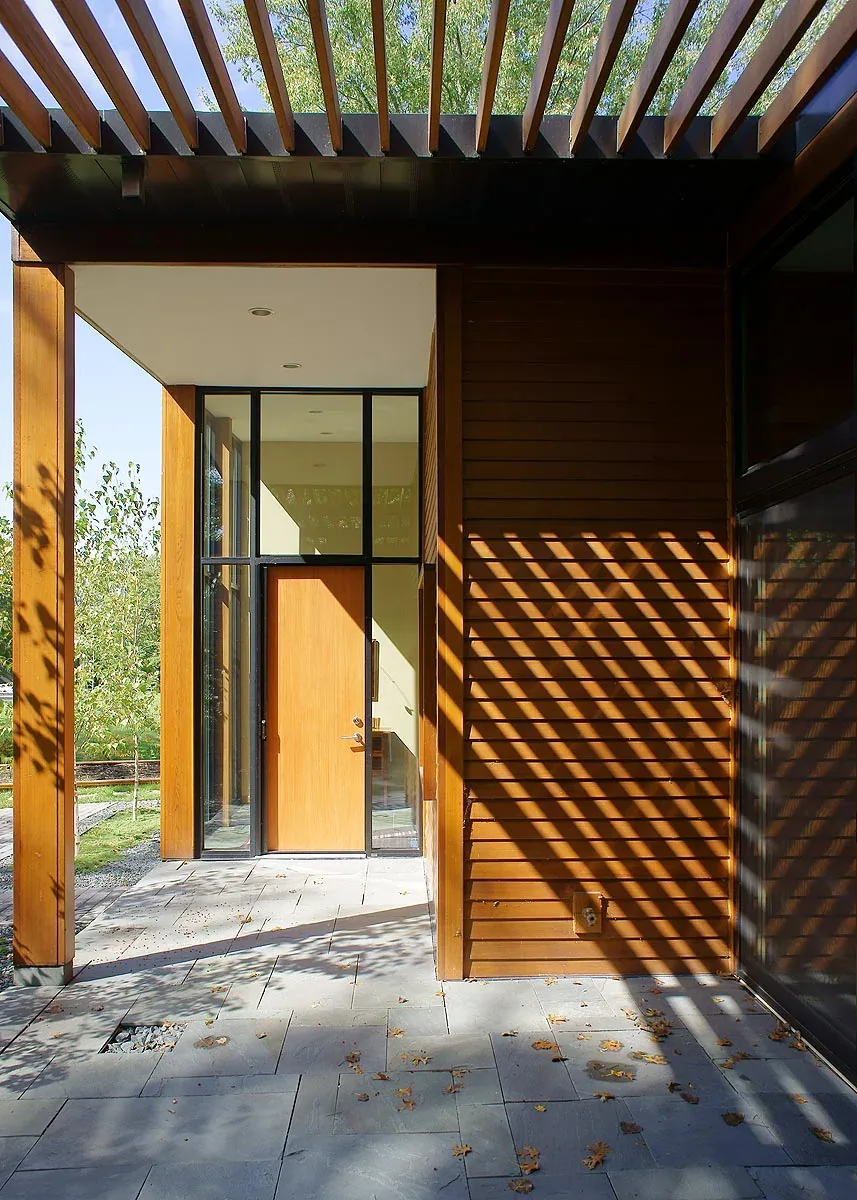 Farquar Lake Residence entry features a wooden door with black-framed glazing and a wood slatted pergola overhead.