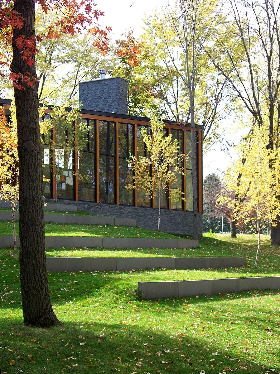 Farquar Lake Residence features a facade with floor-to-ceiling glazing and a stacked stone chimney surrounded by terraced lawn.