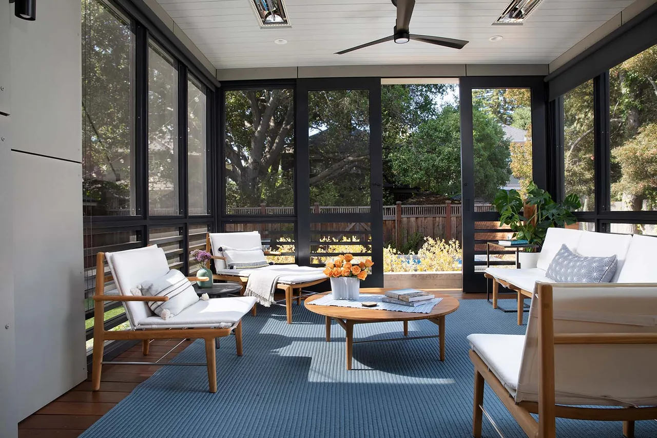 The screened porch features wood framed seating with white cushions, black aluminum window frames, and a wood slat floor.