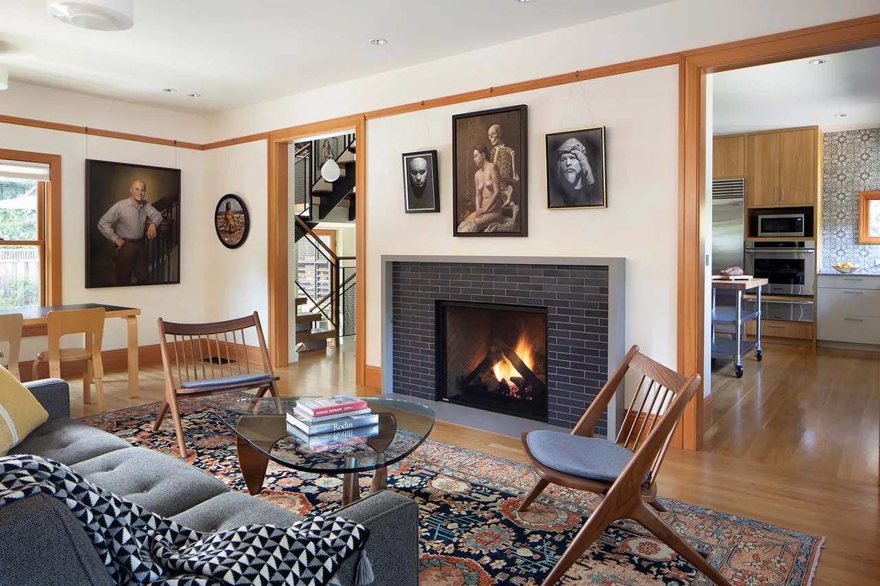 Living room features a black tiled fireplace, wooden trim, vintage-style rug, and midcentury modern chairs, connected to a kitchen.