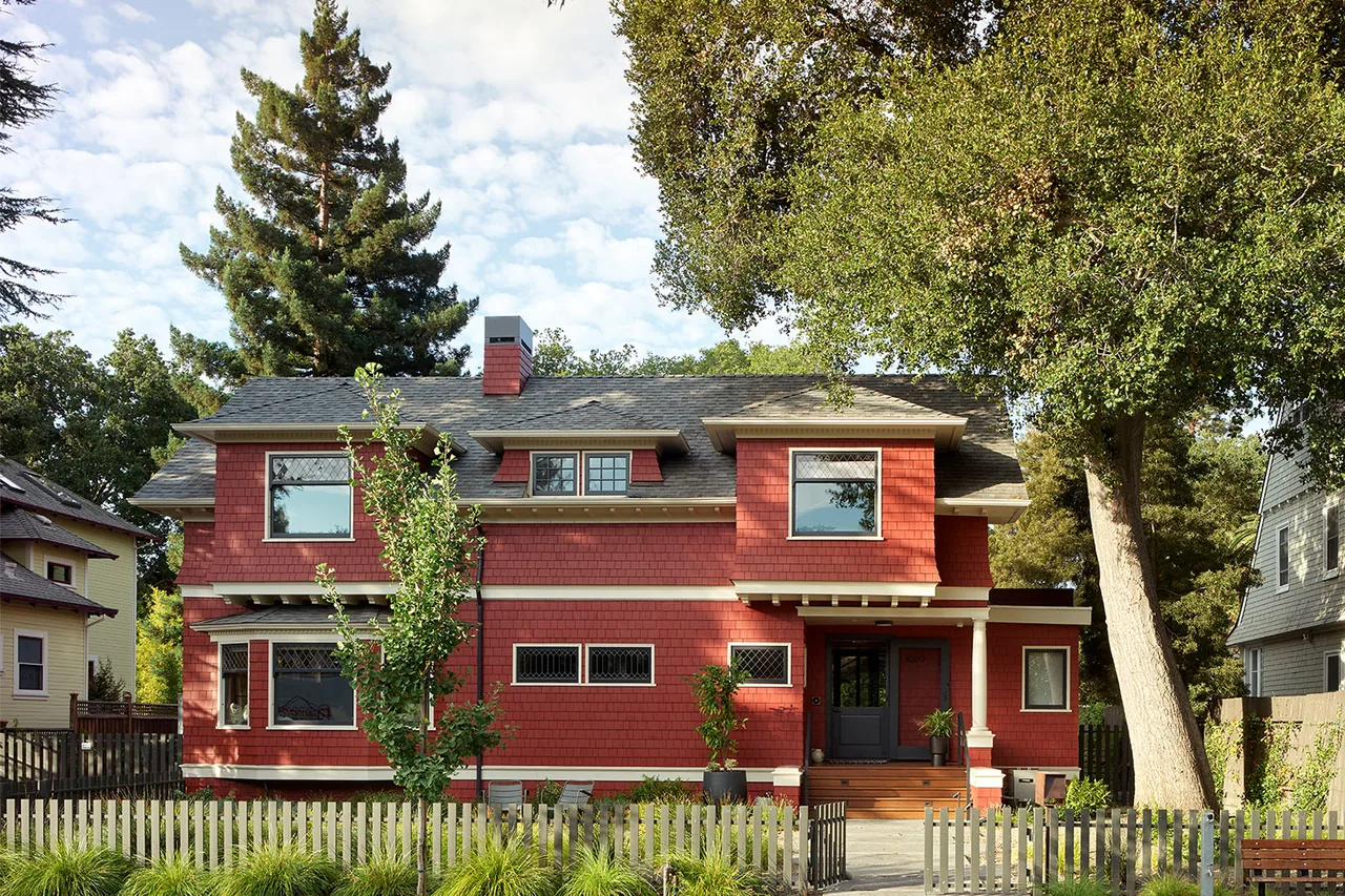 Red two-story home with shingle siding, diamond-pane windows, and a front porch supported by white columns.