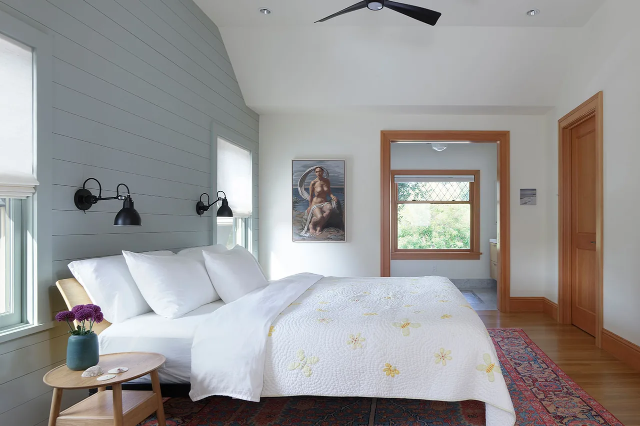 Bedroom featuring painted shiplap accent wall, wooden trim, black wall sconces, and a patterned area rug.