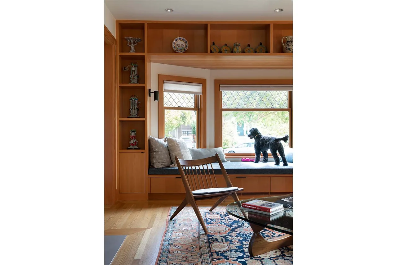 Living room bay window seat with patterned area rug, midcentury style chair, and built-in wooden shelving.
