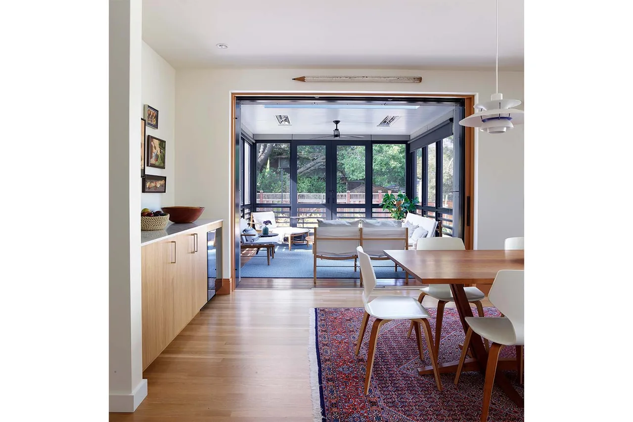Dining area connects to a screened porch through wide sliding glass doors revealing outdoor seating and landscape.