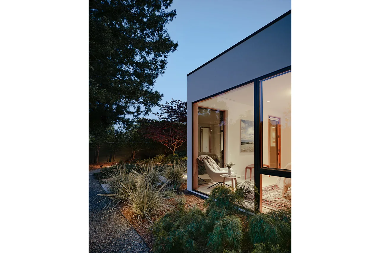 Modern home with large corner windows reveals a cozy indoor seating area and lush landscaping outside.