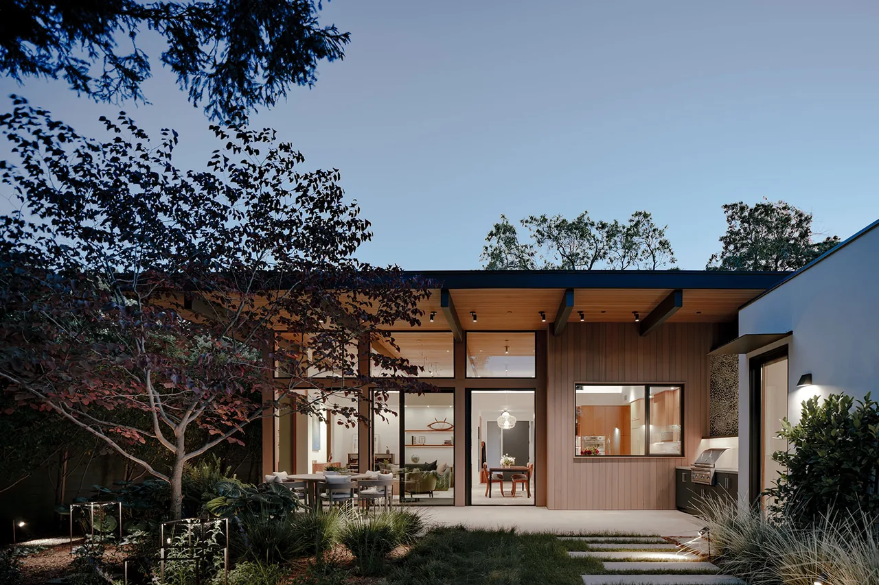 Modern home exterior at dusk with glass entry door, wood vertical slats, and outdoor lighting.