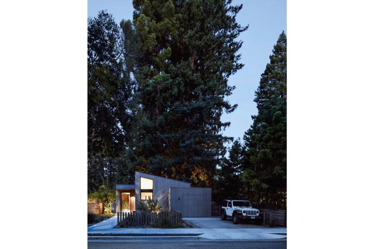 Exterior front view of the eight tree eight house with wood siding and a sloped roof under tall trees at dusk.