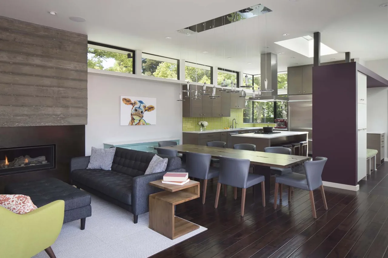 Interior view of open living, dining, and kitchen with concrete chimney, yellow tile backsplash, and purple accent wall in the Moto House.