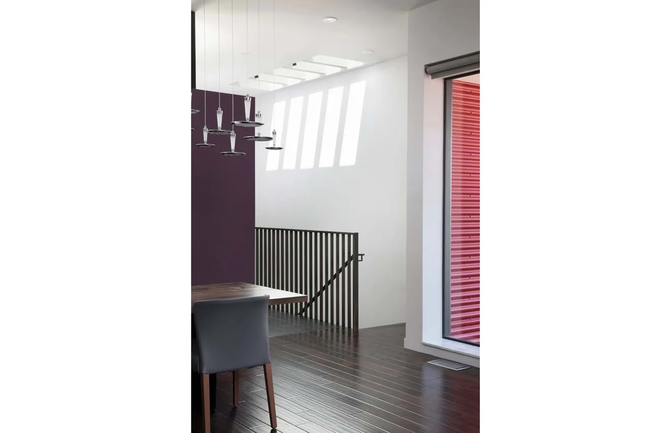 Dining area features dark hardwood flooring, black vertical metal balusters, and a large window showing red siding outside.