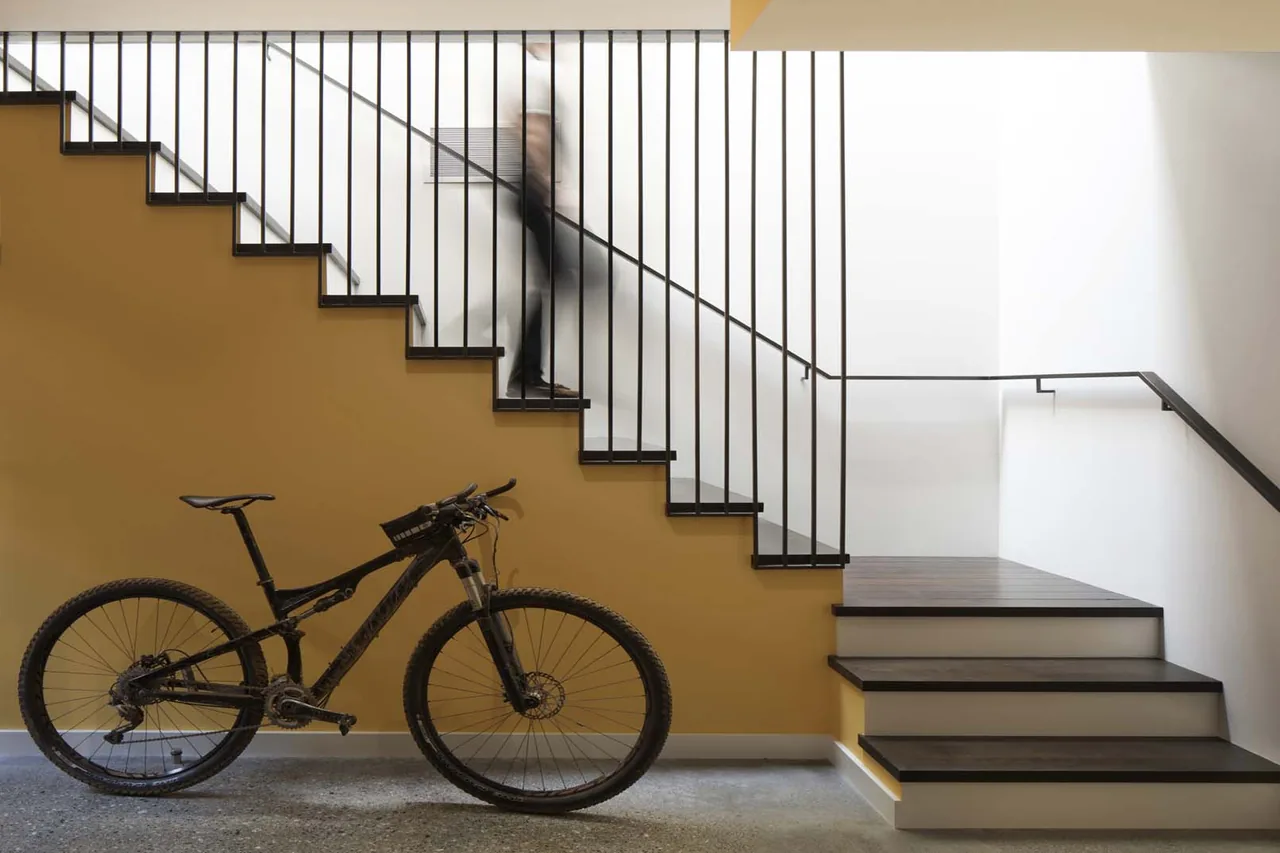 Interior view of a staircase with a yellow accent wall and black vertical railing alongside a black mountain bike.
