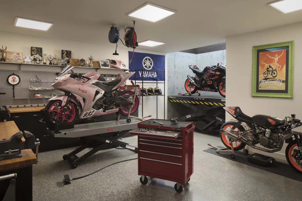 Motorcycle garage space with lifts, tool storage, and display shelves at the moto house project by Ana Williamson Architect.