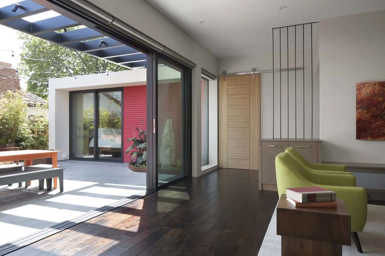 Open living area with green chairs and a large sliding glass door opening to a patio with red accent siding.
