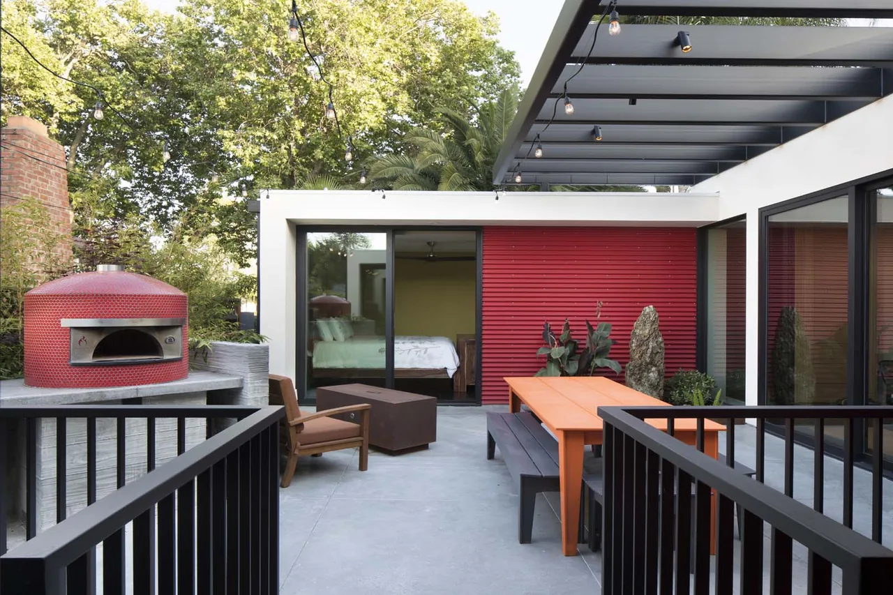 Outdoor living space featuring a pergola roof, orange picnic table, and a red-tiled pizza oven near bedroom sliding doors.
