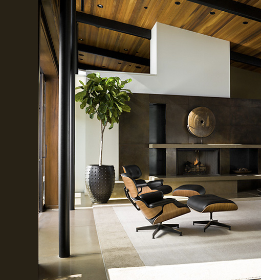 Living space featuring an Eames-style lounge chair and ottoman near a modern fireplace and large potted plant.