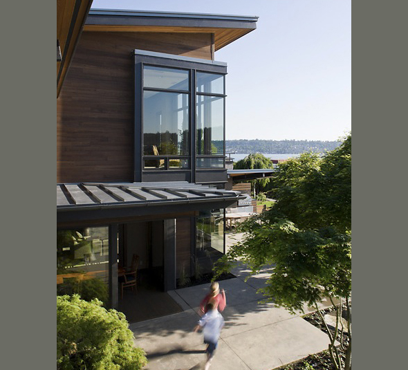 The Porter Residence features wood siding and large black-framed windows with a view to water in the distance.