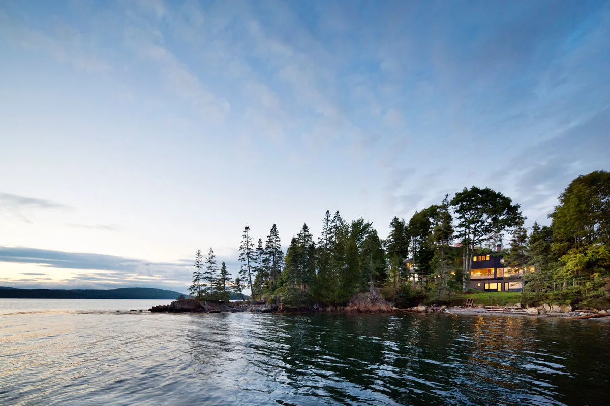 Islesboro Residence features a modern architectural style with wood siding, situated on a wooded waterfront lot.