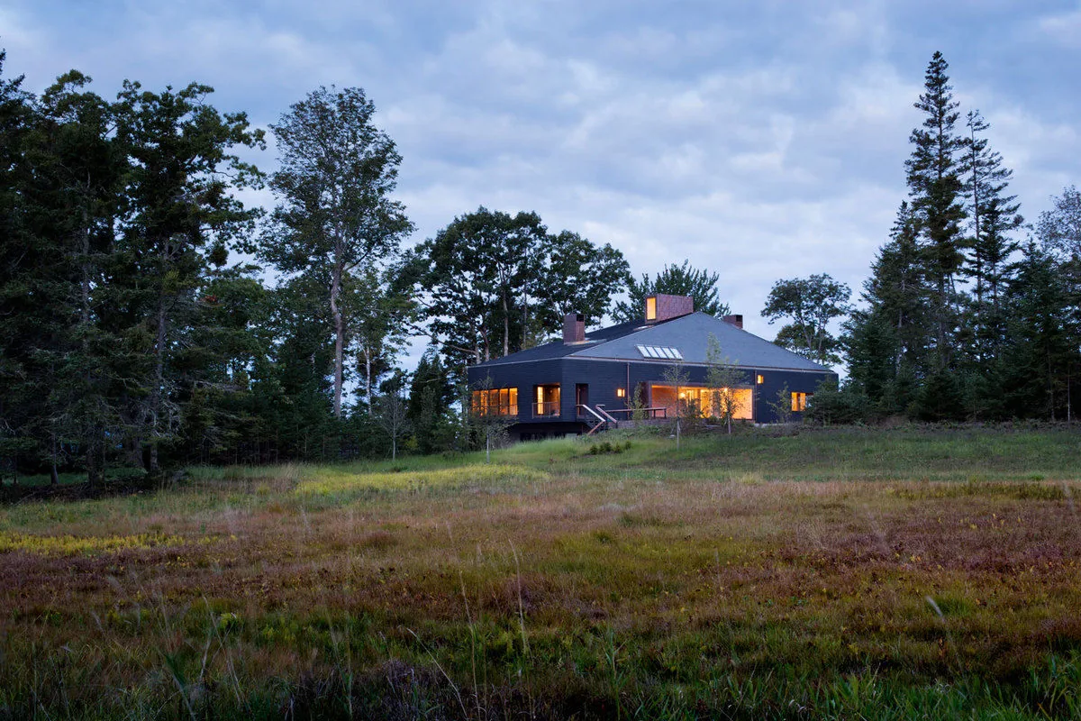Islesboro Residence by Andrew Berman Architect features a dark exterior on a rural site with surrounding trees and meadow.