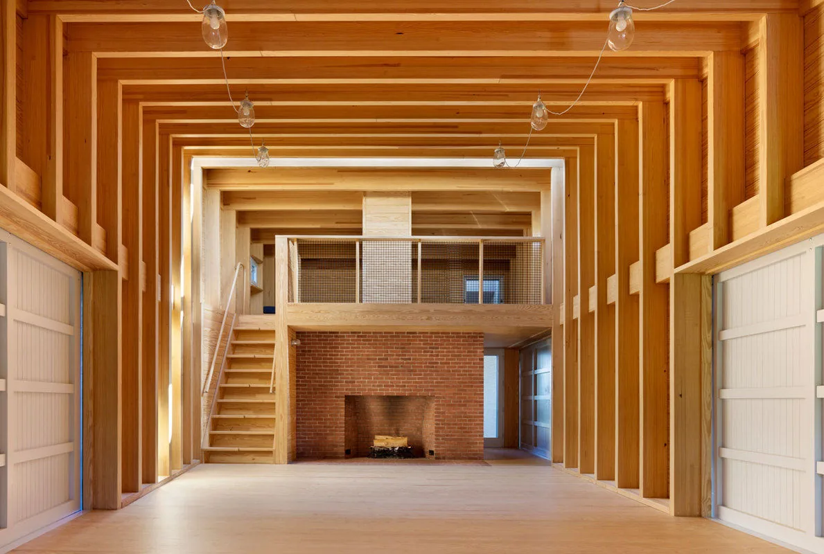 Interior view of the Islesboro Boathouse and Studio featuring exposed wooden beams and a brick fireplace.