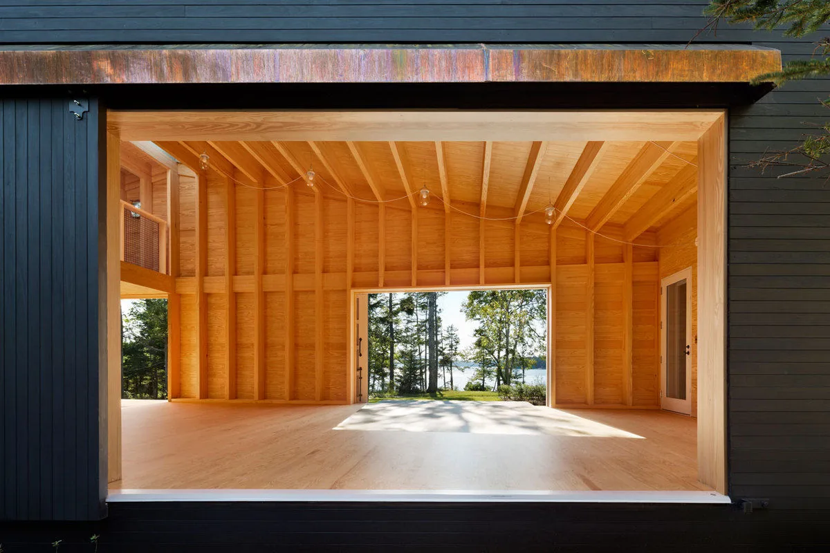 The Islesboro Boathouse and Studio features an open wooden interior with repetitive framing and views to the lake.