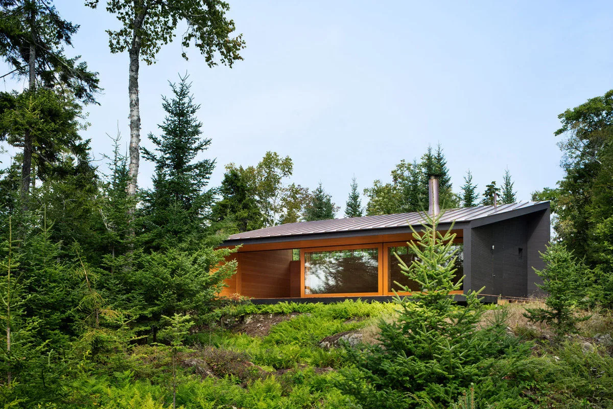 Islesboro Boathouse and Studio features black painted siding, wood paneling, and a simple gable roof in a forest setting.