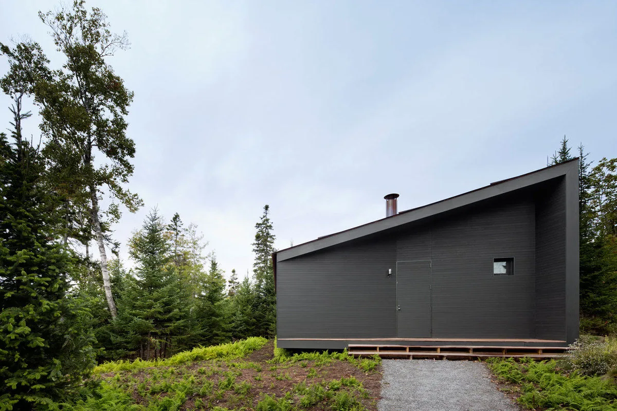 The Islesboro Boathouse features horizontal dark wood siding and a sloped roof, surrounded by forest vegetation.