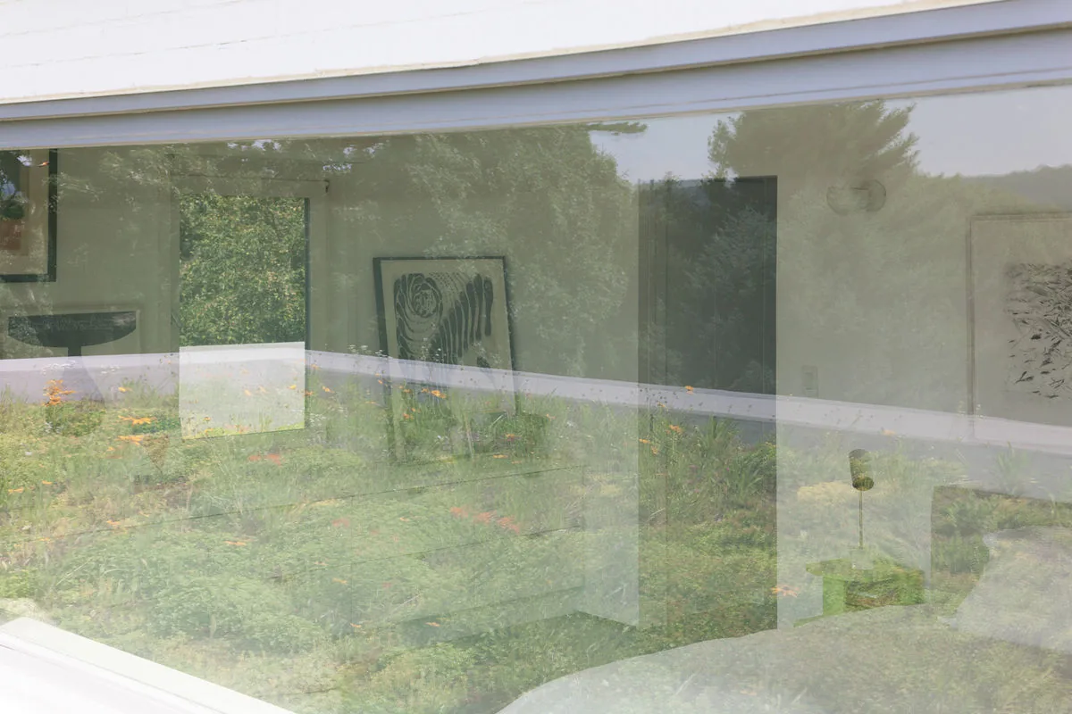 The large window offers a view into the bedroom while reflecting the landscaped front yard outside at Riverdale Residence.